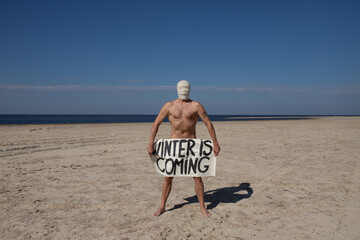 
Naked man in gas mask standing on a deserted beach, holding signs.