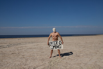 
Naked man in gas mask standing on a deserted beach, holding signs.