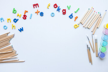 Colorful alphabet magnets and art supplies on white background