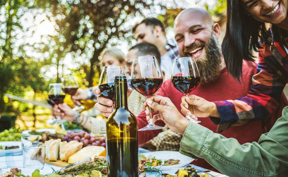 Happy friends having bbq dinner party in garden restaurant - Cheerful family drinking red wine together sitting at dining table - Food and beverage concept with guys and girls eating fresh meal
