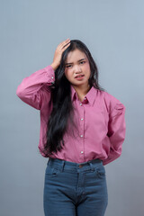 Portrait of an Indonesian woman in a pink shirt touching her head and expressing stress or...