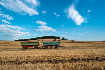 Two green trailers on harvested field under blue sky