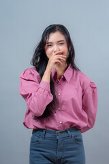 Indonesian woman with long black hair wearing a pink blouse and jeans, standing in studio with a...