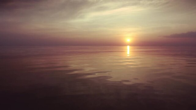 A peaceful sunset over the calm sea. Vibrant orange and blue gradient sky reflects on still water. Minimalist seascape filmed at twilight, ideal for background or meditative footage.