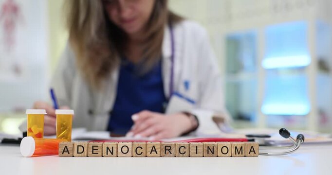 Wooden blocks display Adenocarcinoma word near capsule bottles on doctor desk. Oncologist writes notes planning treatment for glandular cancer type