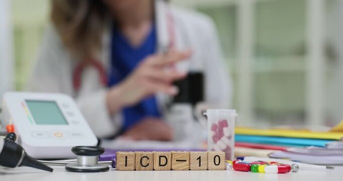 Wooden cubes form ICD-10 word on desk near blood pressure monitor. Medical coder works on disease classification writing diagnostic codes at table