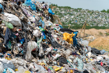 Trash piles high at a landfill with various plastic bags and items scattered across the ground...