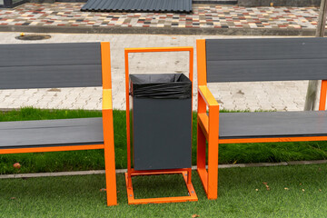 Newly designed benches with bright orange accents flank a black trash can in a well-maintained...