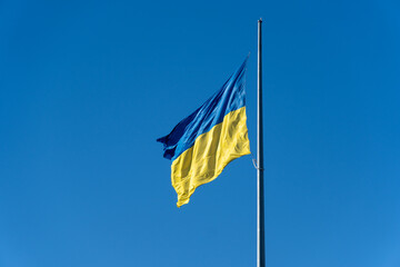 A vibrant Ukrainian flag flutters against a bright blue sky, proudly displayed on a flagpole during a sunny day, symbolizing national pride