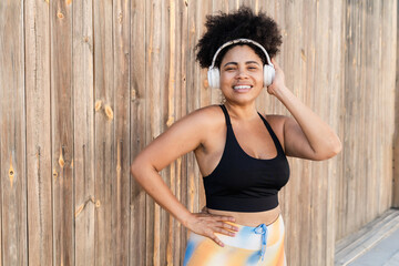 Plus size Latin woman listening music with wireless headphones before sport training outdoors