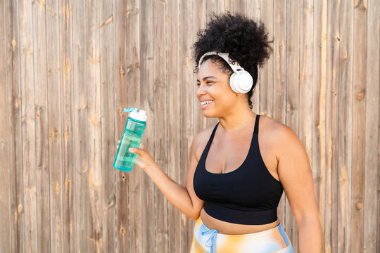 Curvy Latin woman in sportswear and headphones taking a break drinking water after sport training