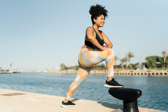 Latin plus-size woman in sportswear stretching legs after running workout by the sea