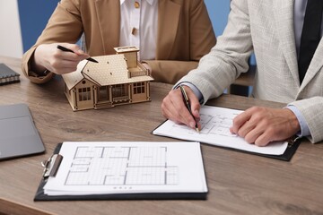 Real estate agent working with client at desk with house model in office, closeup