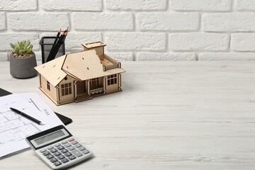 Real estate. House model, floor plan and calculator on white wooden table. Space for text