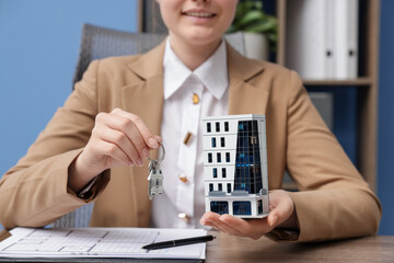 Real estate agent holding key and house model at desk in office, closeup