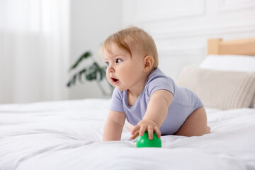 Cute little baby with toy on bed at home, space for text