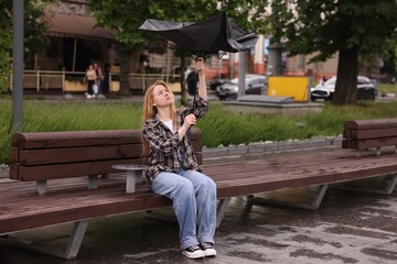 Woman with broken umbrella on bench outdoors