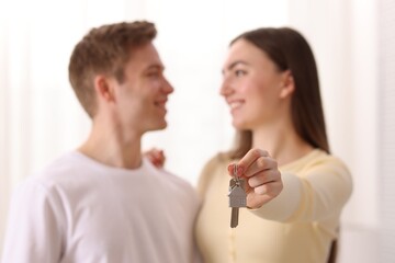 Happy couple with key of their new house indoors, selective focus