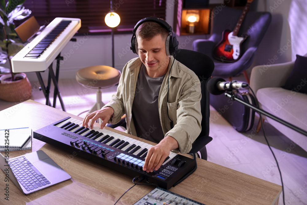 Poster man in headphones working with midi keyboard at table in home studio