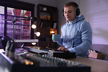 Man in headphones working with MIDI keyboard at table in home studio, low angle view