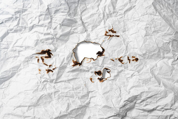 Burnt hole on crumpled sheet of white paper on a white background. Creased and wrinkled paper...
