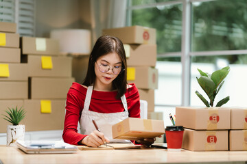 Young Asian woman in red shirt and apron doing online business, multitasking between smartphone and...