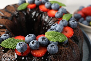 Delicious chocolate bundt cake with strawberries, mint and blueberries on table, closeup