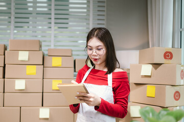 Young Asian woman in red shirt and apron running her online business, multitasking between...