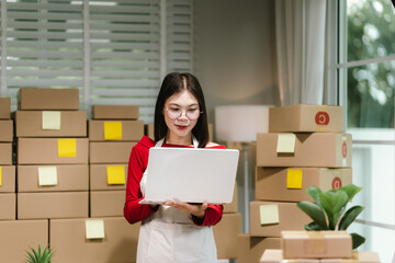Young Asian woman in red shirt and apron doing online business, multitasking between smartphone and...