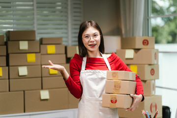 Young Asian woman in red shirt and apron running her online business, multitasking between...