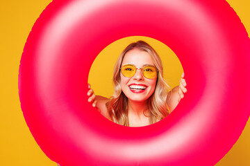 Close up young happy beautiful sexy woman wear bikini swimsuit rest near hotel pool hold in hand look through pink rubber ring isolated on plain yellow background. Summer vacation sea sun tan concept.