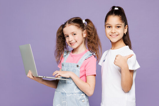 Little fun two friends kids children IT girls 9-10 years old wear casual clothes together hold use work on laptop pc computer point finger aside isolated on plain purple background. Lifestyle concept. - Powered by Adobe