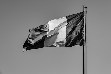 National flag of Romania flying in the wind; black and white version of the red yellow and blue flag on clear sky background