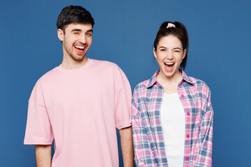 Fototapeta premium Young smiling happy cheerful satisfied positive couple two friends family man woman they wear pink casual clothes together look camera blink wink eye isolated on plain blue background studio portrait.