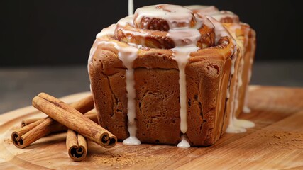 Pouring sweet white icing glaze on a freshly baked cinnamon roll loaf on a wooden board with cinnamon sticks - Powered by Adobe