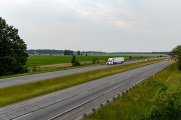 Truck drives down highway beside field.