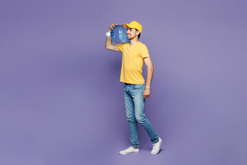 Full body side view young delivery guy employee man in yellow cap t-shirt uniform workwear work...