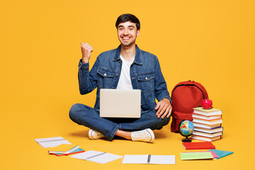 Full body young boy IT student wear jeans casual clothes sit near backpack bag books use laptop pc...