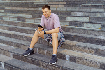 Smiling man using smartphone on stone steps in summer outfit