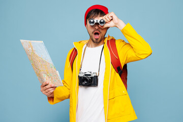 Traveler man wear yellow casual clothes read paper map use binocular isolated on plain pastel blue background. Tourist travel abroad in free spare time rest getaway. Air flight trip journey concept.