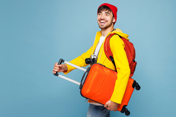 Side view traveler man wear hat yellow casual clothes hold suitcase bag isolated on plain pastel...