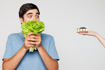 Young man wear blue t-shirt casual clothes hold bunch of lettuce salad cover mouth choose between...