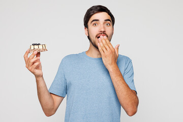 Young shocked scared man wear blue t-shirt casual clothes hold in hand eat piece of cake cover...