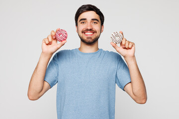 Young smiling fun man wear blue t-shirt casual clothes hold in hand two sweet tasty donuts look...