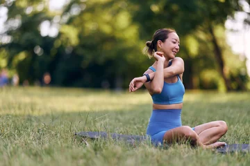 Selbstklebende Fototapeten Entspannung Woman Stretching Outdoors in a Park During Daytime Wearing Blue Fitness Outfit  © bnenin