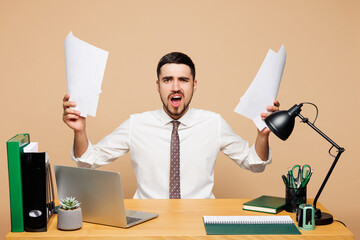 Young angry sad mad dissatisfied employee business man wear white shirt tie sit work at office desk...