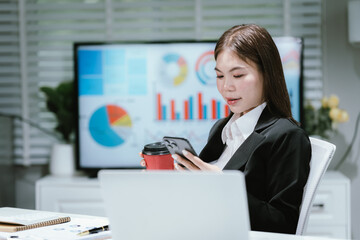 A professional businesswoman works at her desk, analyzing financial documents and charts, writing...