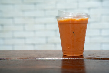 Iced Thai tea in a clear plastic cup with a lid, featuring its signature bright orange color. Condensation on the cup hints at its cold, refreshing quality. Placed on a wooden surface 