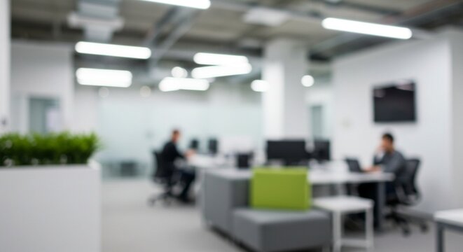 Blurred view of a modern, open-plan office space with people working at desks, featuring white walls, bright lighting, and green accents.