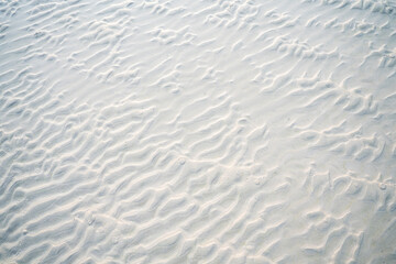Close-up of beach sand texture with natural wave-like patterns and subtle shadows. Perfect background for summer, vacation, and nature-themed designs or creative projects.